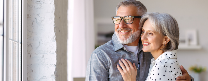 Life Assure Seniors Man And Woman Hugging Looking Out Window Hero